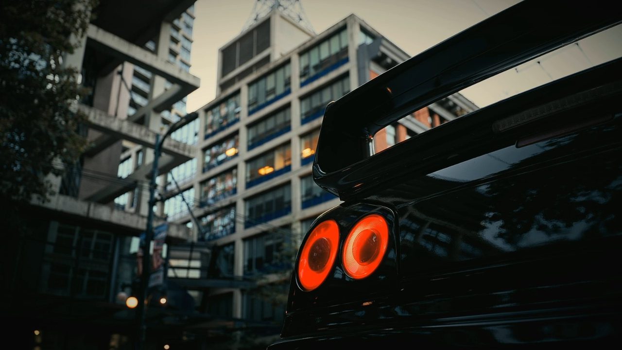 Rear of a dark sports car with round lit taillights and a rear wing at dusk.