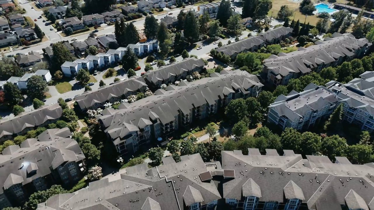 Aerial view over rows of townhouse rooftops and green courtyards.